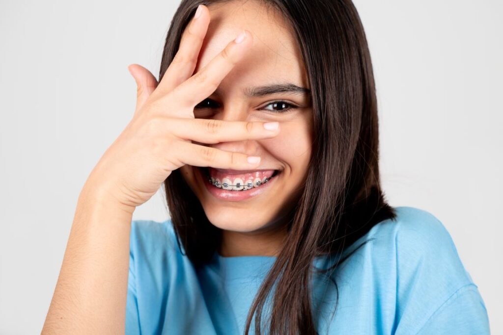 A young girl wearing braces and hiding her face behind her hand.