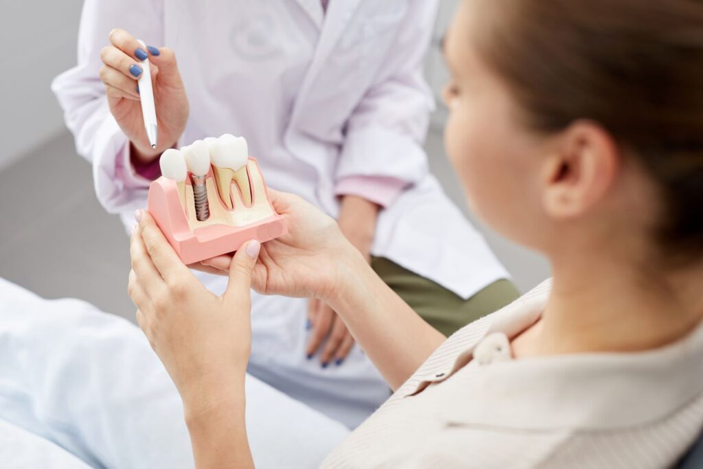 A woman and her dentist looking at a model of a jaw with a dental implant